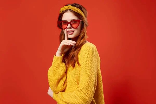 Vrouw in geel trui dragen rode bril hoofdband mode rode achtergrond — Stockfoto