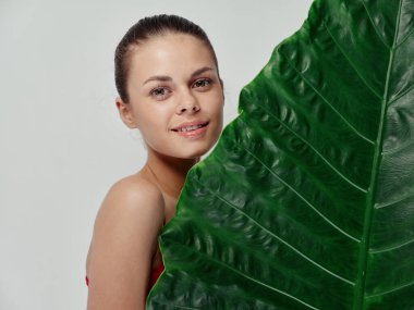 Açık arkaplanda yeşil palmiye yaprağı tutan kadın kırmızı t-shirt 'ü kırpmış.