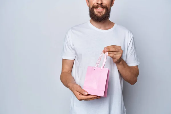 Homme joyeux en t-shirt blanc avec petit paquet rose cadeau fond clair — Photo