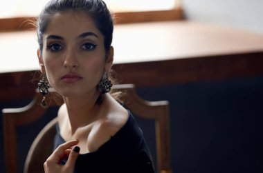 Siyah elbiseli güzel bir kadın sandalyede oturmuş lüks bir hayat sürüyor.