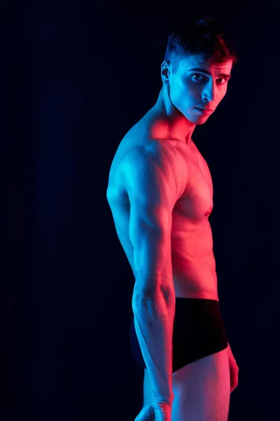 Sexy man met een pomped-up romp poseren op een donkere achtergrond zijaanzicht en neon licht — Stockfoto