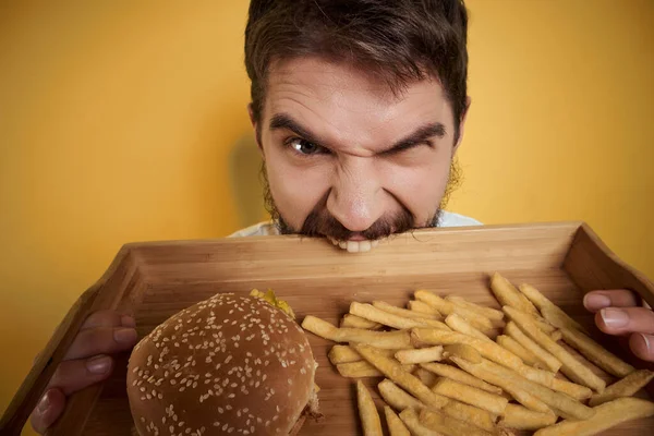 Vousatý muž dřevěný tác s rychlým občerstvením pivo zábava hranolky burgery — Stock fotografie