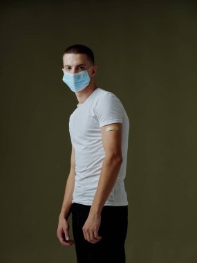 Tıbbi maskeli bir adam ve aşı pasaport modeli beyaz tişörtlü koyu arkaplan