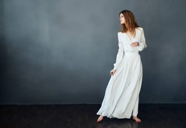 Mulher descalça em um vestido branco dançando em um fundo escuro — Fotografia de Stock