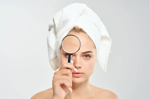 Mujer con una toalla en la cabeza sostiene una lupa cerca del acné facial — Foto de Stock