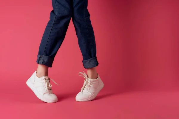 Женские ноги в белых кроссовках в моде, позируя розовый фон — стоковое фото