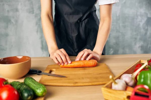 Donna in grembiule nero pranzo a casa tagliere cibo vegetariano — Foto Stock