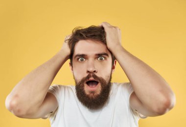 Tişört giymiş yakışıklı bir adam, elleri sarı arkaplanlı bir jest yapıyor.