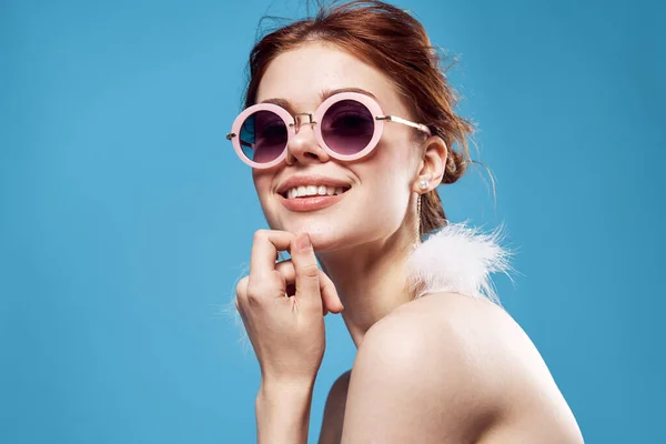 Emotivní žena nosí sluneční brýle nadýchané náušnice šperky close-up modré pozadí — Stock fotografie
