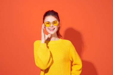 Sarı gözlüklü neşeli kadın başını kırmızı arka planda tutuyor.