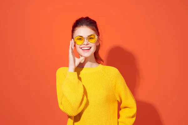 Vidám nő sárga szemüvegben tartja a fejét divat piros háttér — Stock Fotó