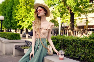 Neşeli kadın yaz tatilinde bir içkiyle parkta yürüyor.