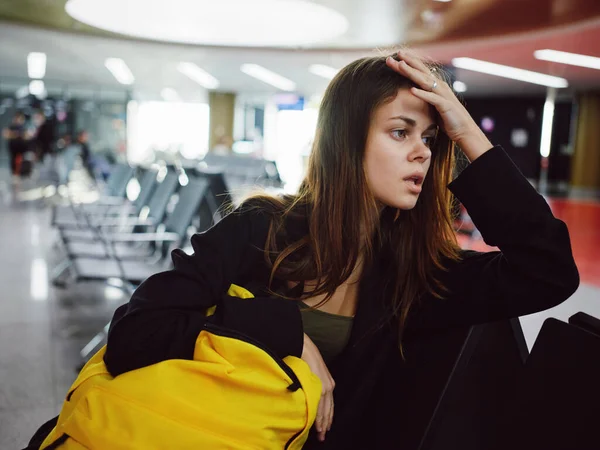 Γυναίκα κρατώντας το κεφάλι της περιμένει αεροδρόμιο κίτρινο σακίδιο κουρασμένος — Φωτογραφία Αρχείου
