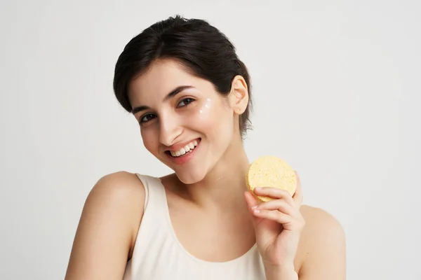 Morena bonita em uma camiseta branca com uma esponja em suas mãos e cosméticos de saúde pele limpa — Fotografia de Stock