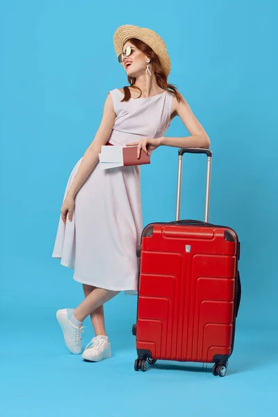 Femme en robe blanche valise rouge destination voyage fond bleu — Photo