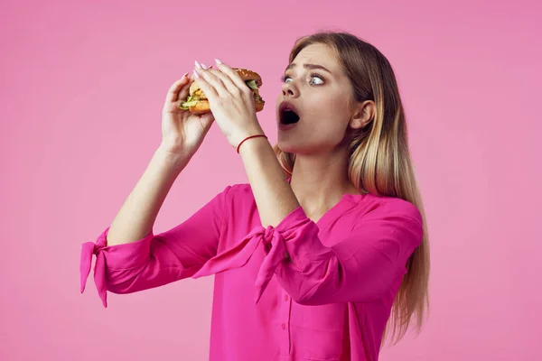 Loira alegre em uma camisa rosa hambúrguer lanche fast food — Fotografia de Stock