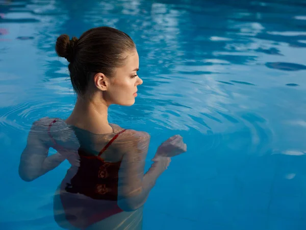 Mujer bonita en traje de baño se encuentra en la baldosa de la piscina en vista trasera de agua transparente —  Fotos de Stock