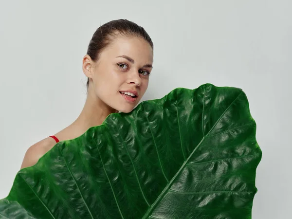 Mujer sosteniendo delante de su hoja de palma escondida detrás de hombros desnudos fondo claro —  Fotos de Stock