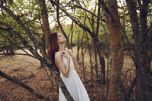 Pretty woman in white dress leaning on a tree in the summer forest. High quality photo