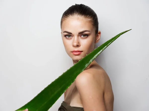 Jovem com ombros nus segurando folha de aloés verde na frente de seu rosto — Fotografia de Stock