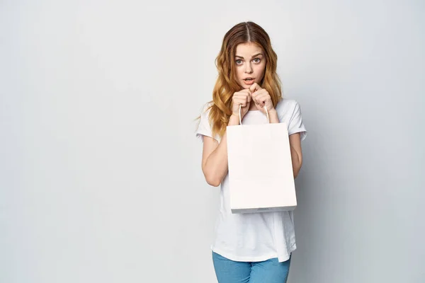 Mujer en una camiseta blanca con un paquete en sus manos un regalo Compras fondo claro — Foto de Stock