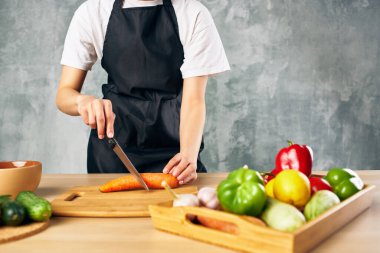 Mutfakta siyah önlüklü bir kadın sebze doğruyor salata vitamini pişiriyor.