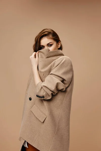 Mulher de casaco cobre o rosto com gola e bege modelo de fundo — Fotografia de Stock