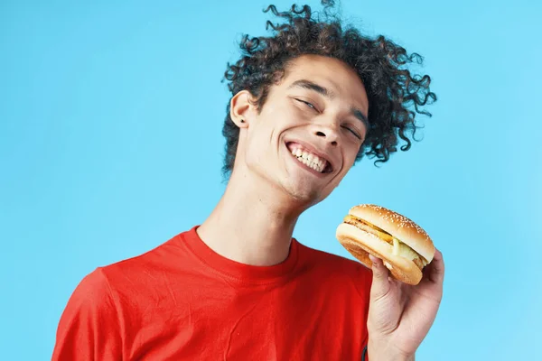 빨간 티셔츠 햄 버거 패스트 푸드 블루 배경에 곱슬머리의 남자 — 스톡 사진