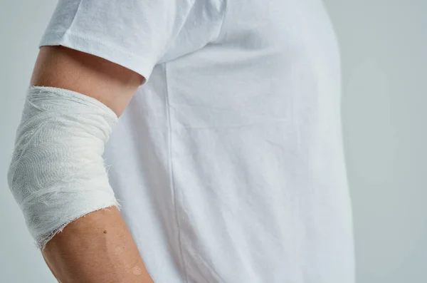 Paciente do sexo masculino em uma camiseta branca com uma mão enfaixada fundo isolado — Fotografia de Stock
