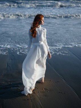 Beyaz elbiseli kadın plaj tatilinde yürürken poz veriyor.