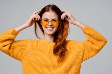 Sarı süveterli, kırmızı saçlı bir kadın. Moda gözlüğü takıyor.