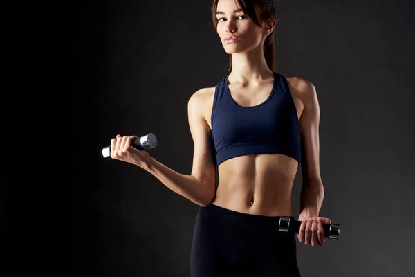 Atletik kadın, halterlerle meşgul. Güç egzersizleri, karanlık arka plan egzersizleri. — Stok fotoğraf