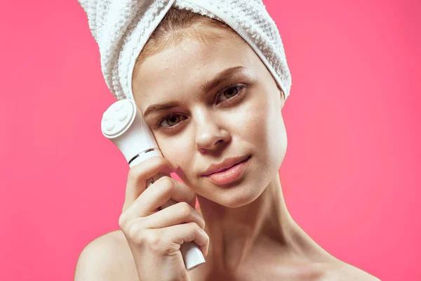 Kvinna med handduk på huvudet rengöring ansikte hudvård rosa bakgrund — Stockfoto