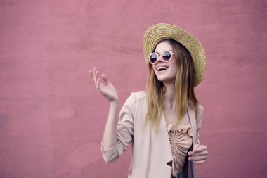 Güzel bir kadın sokakta şapka ve gözlük takıyor. Pembe duvar modeli.