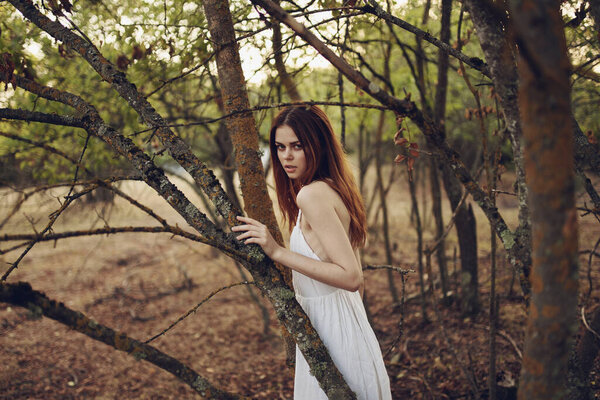 Pretty woman in white dress leaning against a tree