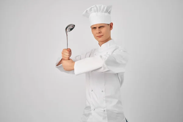 Un uomo in uniforme chef con un mestolo in mano preparare cibo sfondo luce — Foto Stock