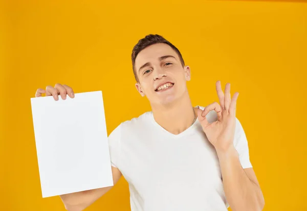 Mann in weißem T-Shirt leeres Blatt Papier Präsentation gelb Hintergrund — Stockfoto