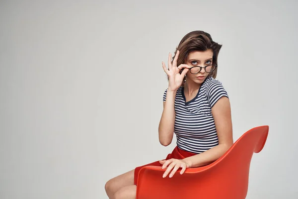 Kırmızı sandalyede oturan çizgili tişörtlü kadın modern saç stili. — Stok fotoğraf