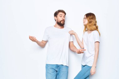 Beyaz tişörtlü ve kot pantolonlu neşeli adam ve kadın stüdyo ışık arka planı tasarlıyor.