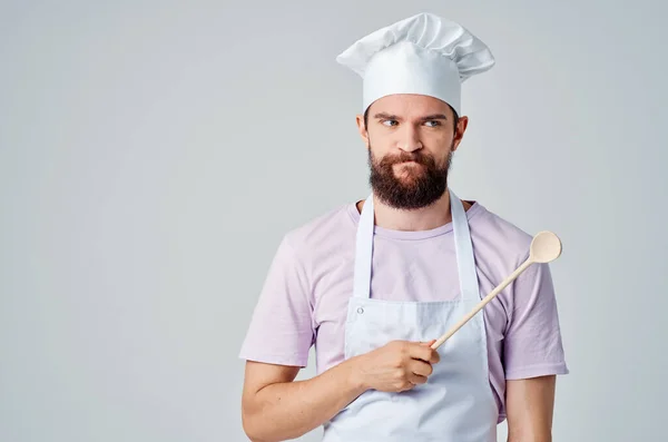 Chef masculino em um avental branco com um boné na cabeça com uma colher em suas mãos preparando comida — Fotografia de Stock