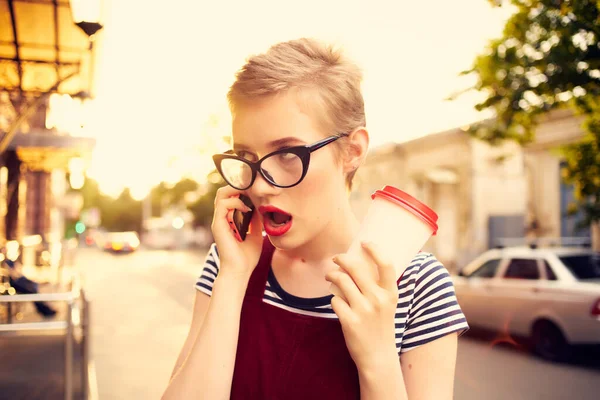 Kvinna med glasögon talar i telefonen på gatan en kopp kaffe Stockbild