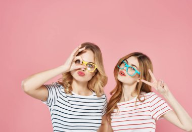 Çizgili tişörtlü, pembe arka plan pozu veren neşeli moda kızlar.