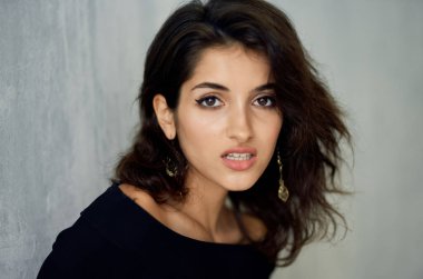 Saçları dağınık güzel bir kadın duvarın yanında poz veriyor.