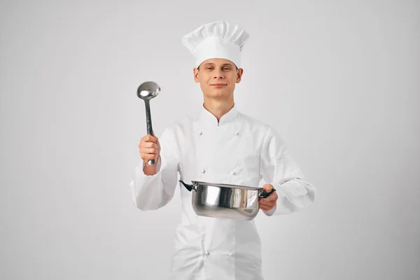 Un uomo in uniforme da chef con una padella e un mestolo in mano che prepara il cibo — Foto Stock