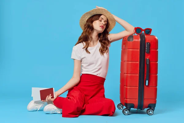 Žena s červeným kufříkem sedí na podlaze modré pozadí cestování dovolená — Stock fotografie