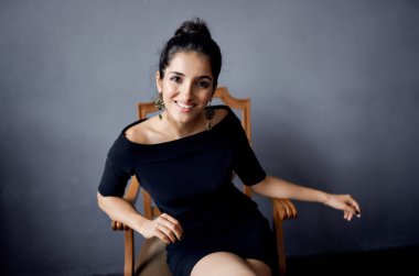 Sandalyenin yanındaki siyah elbiseli güzel kadın lüks moda izole edilmiş arka plan.