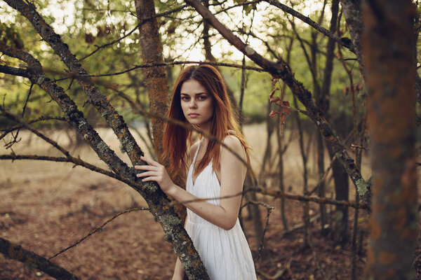 Red-haired Woman in a white dress in the forest trees fallen leaves. High quality photo