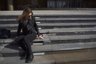 Deri ceketli kadın açık hava tatili için bina yakınında.