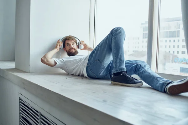 Cute man lying near the window wearing headphones fun — Stock Photo, Image