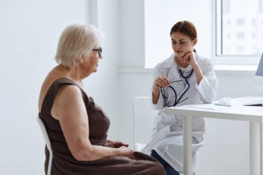 Tıp bürosundaki doktorlar yaşlı bir kadın sağlık kontrolüyle konuşuyorlar.